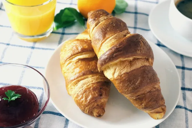 Two butter croissants on a plate with jam and orange juice