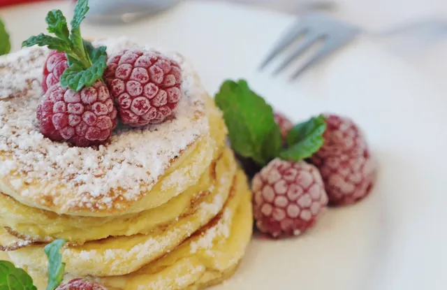 A stack of pancakes topped with raspberries, mint and powdered sugar