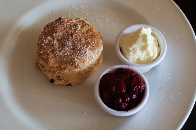 A scone with a dish of jam and a dish of cream